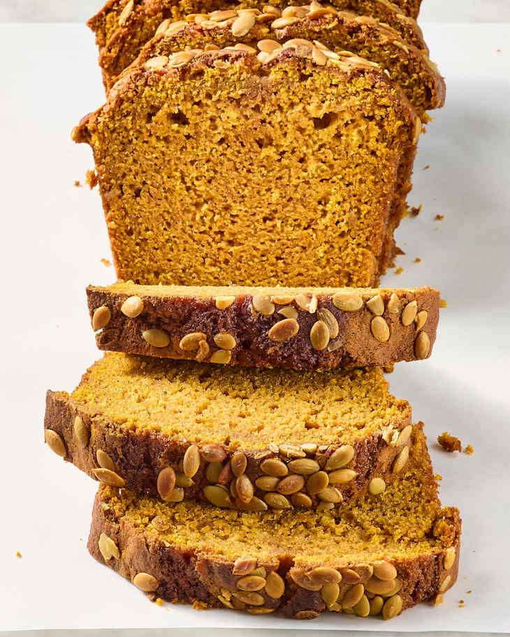 Sliced pumpkin bread topped with pumpkin seeds, showcasing a moist texture and golden color.