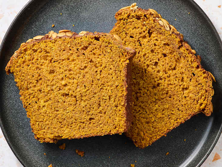Sliced pumpkin bread on a black plate, showcasing a moist texture and topped with pumpkin seeds.