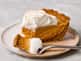 Slice of pumpkin pie topped with whipped cream on a speckled plate, with a fork resting beside it.