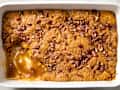 A white baking dish of pumpkin pecan cobbler with a  scoop taken out
