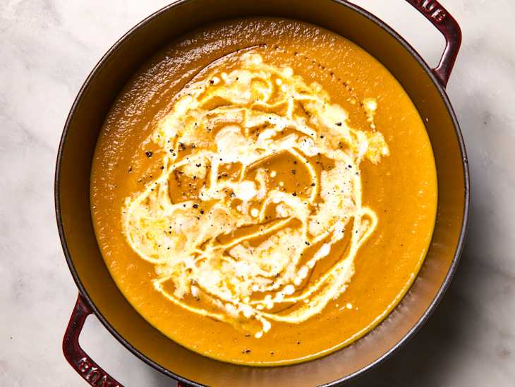 Creamy orange soup in a deep pot, swirled with cream and topped with black pepper.