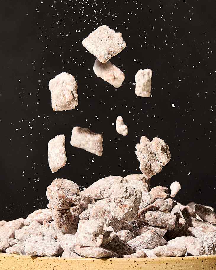Chunks of textured rock salt suspended above a pile, with fine particles scattering in the air.