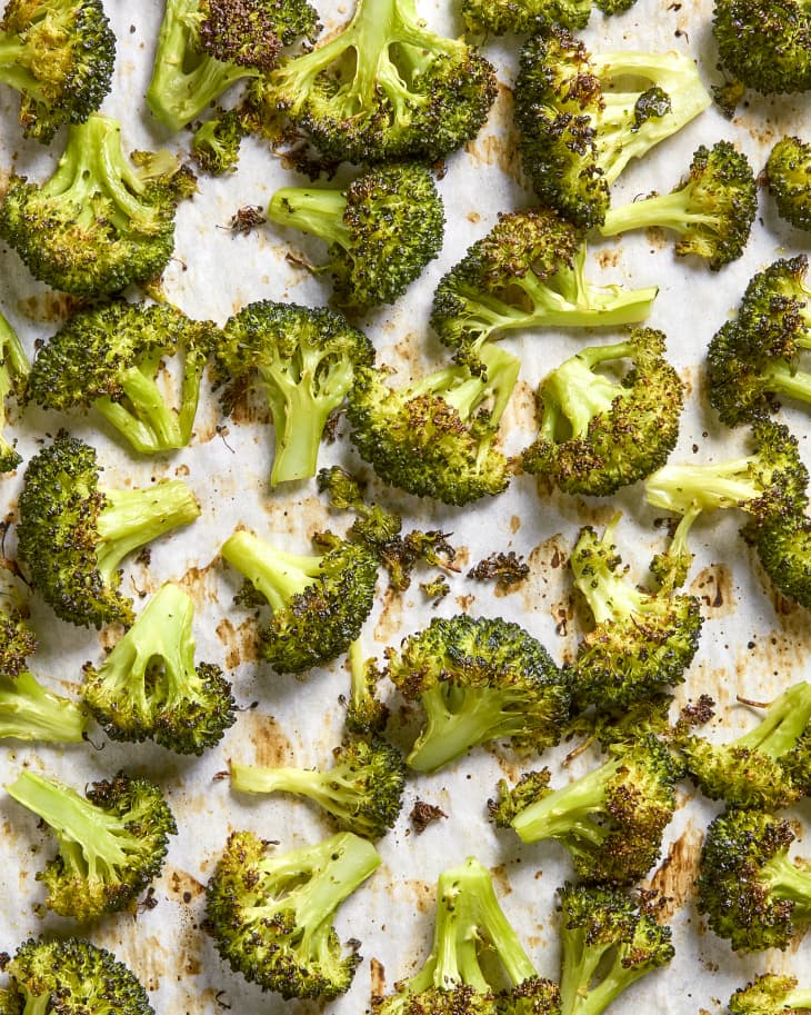 Overhead shot of roasted broccoli on white parchment paper, in a sheet pan.
