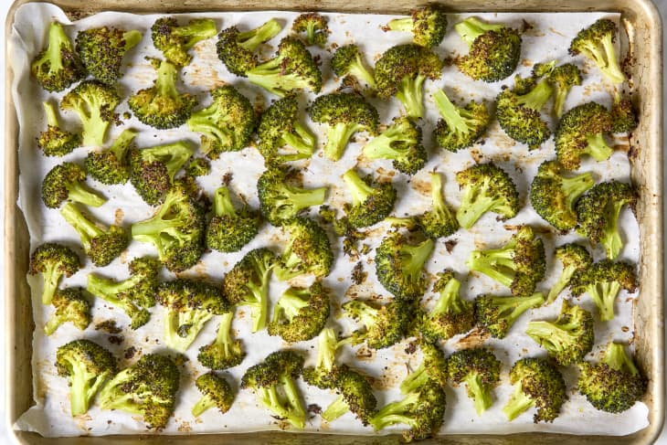 Overhead shot of roasted broccoli on white parchment paper, in a sheet pan.