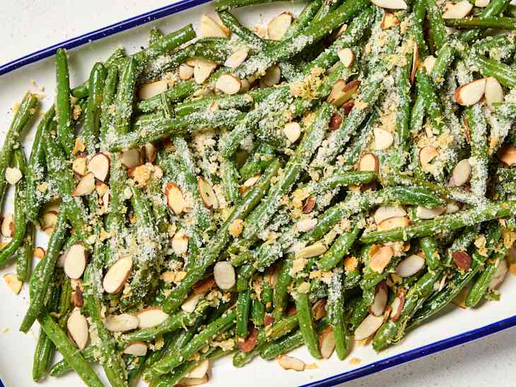 A platter of roasted green beans with almonds, parmesan cheese, and breadcrumbs on top
