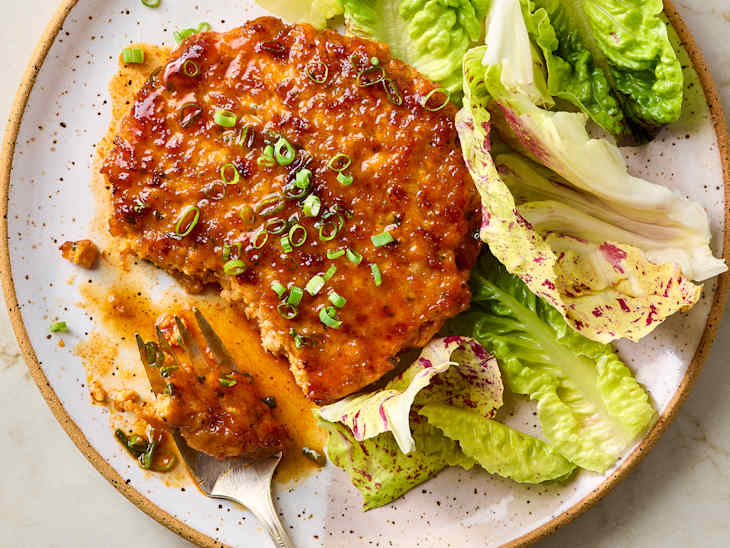 A glazed salmon cake topped with chopped green onions, served with fresh romaine and colorful lettuce leaves.