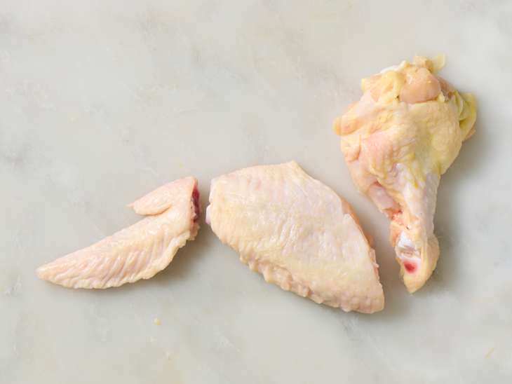 Raw chicken wings and drumette pieces arranged on a light marble surface.