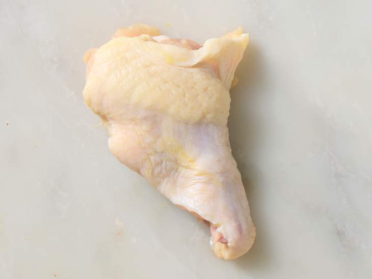 Raw chicken drumstick on a light marble surface, showcasing its skin texture and shape.
