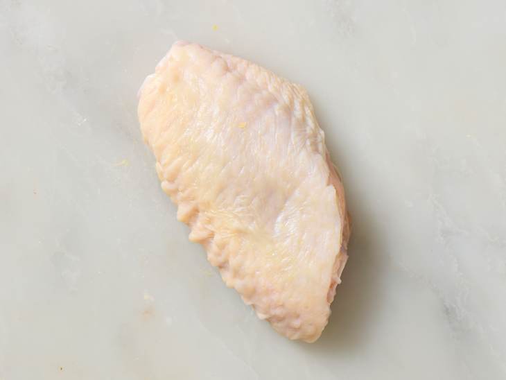 Raw chicken wing piece on a light marble surface, showcasing its smooth texture and natural color.