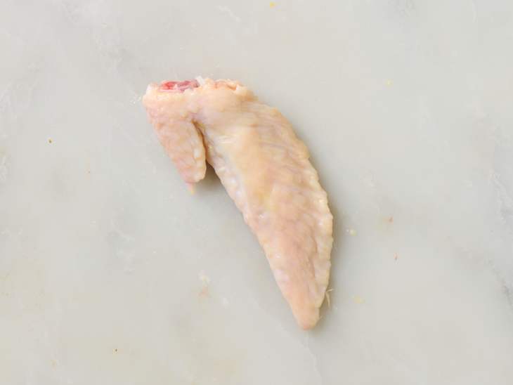 Raw chicken wing on a light marble surface, showcasing its texture and shape.