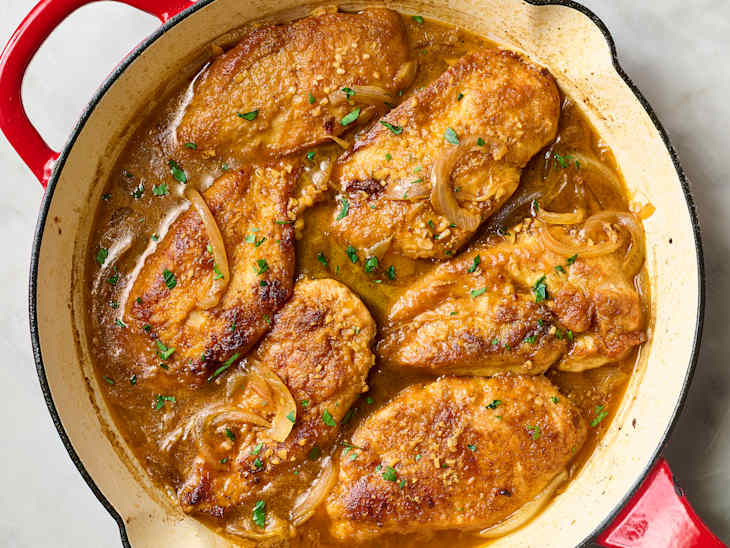 Pan-seared chicken fillets in a rich sauce with onions and parsley, served in a red Dutch oven.