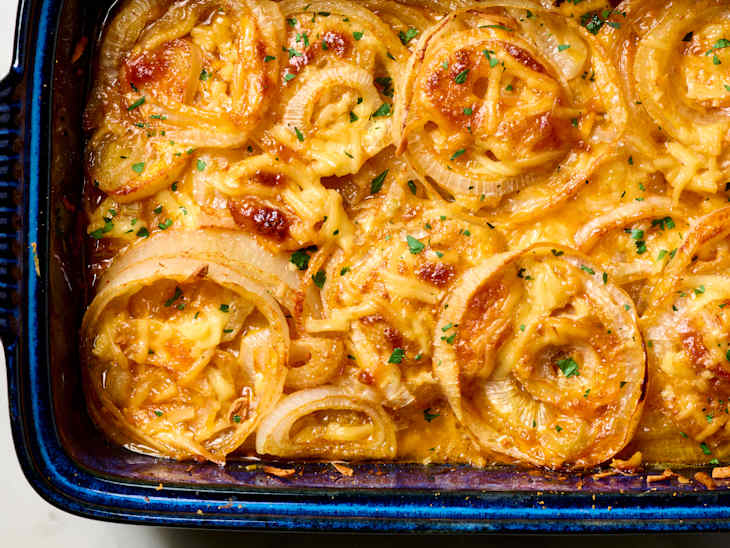 Baked dish with layers of cheese, caramelized onions, and herbs in a blue casserole dish.