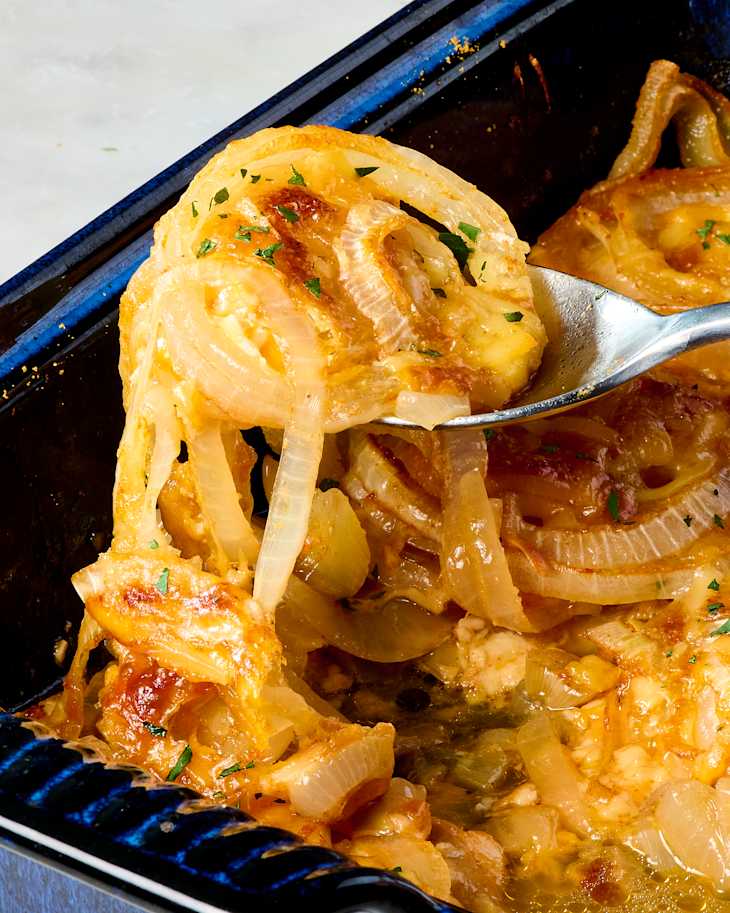 Baked dish with caramelized onions, cheese, and herbs, served in a blue dish with a spoon.