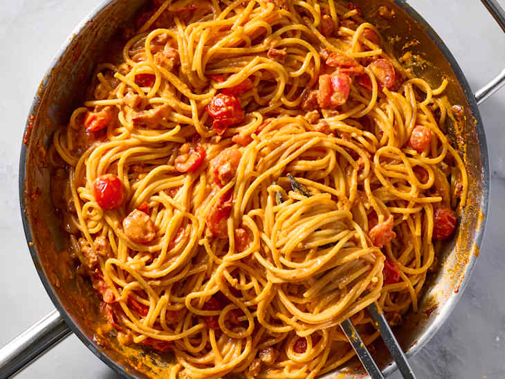 Spaghetti mixed with cherry tomatoes and crumbled cheese in a skillet, garnished with black pepper.
