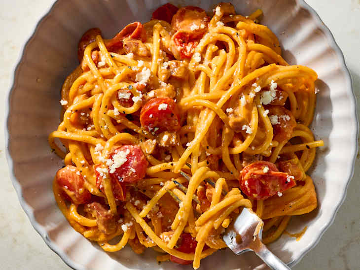 Spaghetti mixed with cherry tomatoes and crumbled cheese in a skillet, garnished with black pepper.