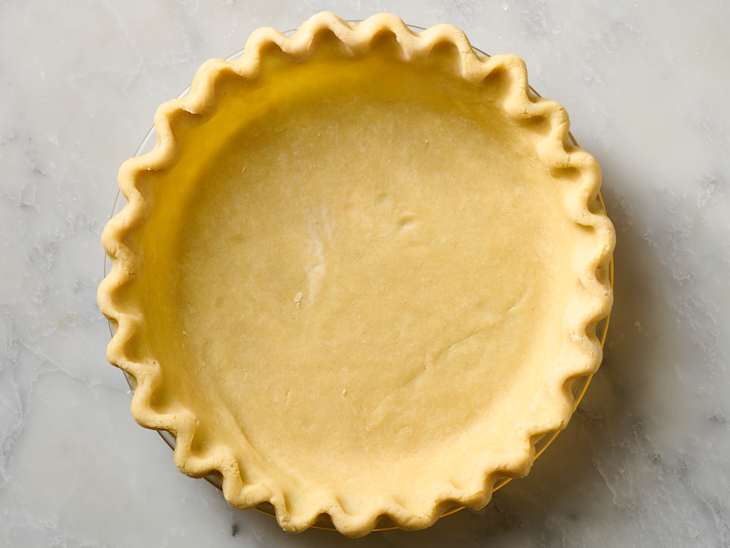Unbaked pie crust in a fluted pie dish on a marble surface.