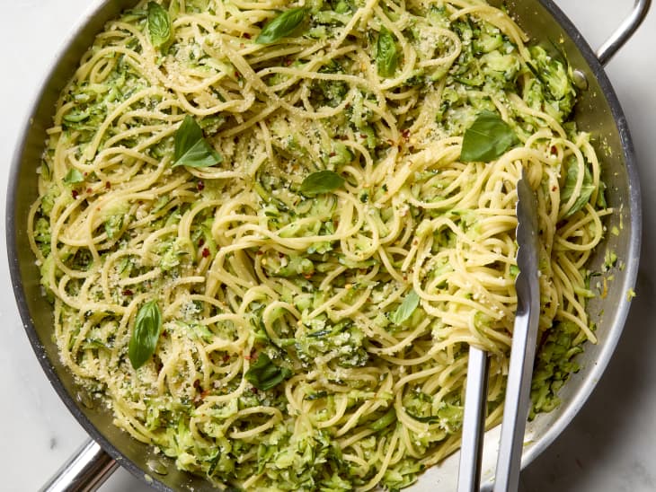overhead shot of zucchini butter pasta in a silver pan, with tongs grabbing some out of the pan